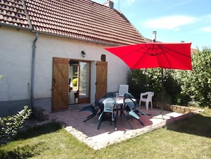 Eine Terrasse mit Tisch und Stühlen, einem roten Sonnenschirm und einem Haus mit Ziegeldach.