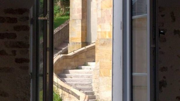 A stone staircase leading to a door, with a view of greenery outside.