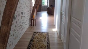 A hallway with exposed wooden beams, a patterned rug, and a staircase leading to another room.