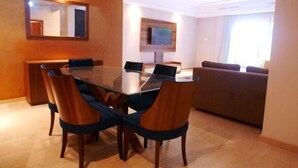 Zona pranzo moderna con tavolo in vetro, sedie in legno e un divano sullo sfondo.