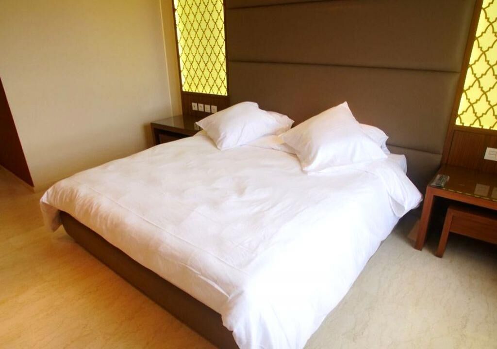 A neatly made bed with white linens in a room with wooden flooring and a brown headboard.