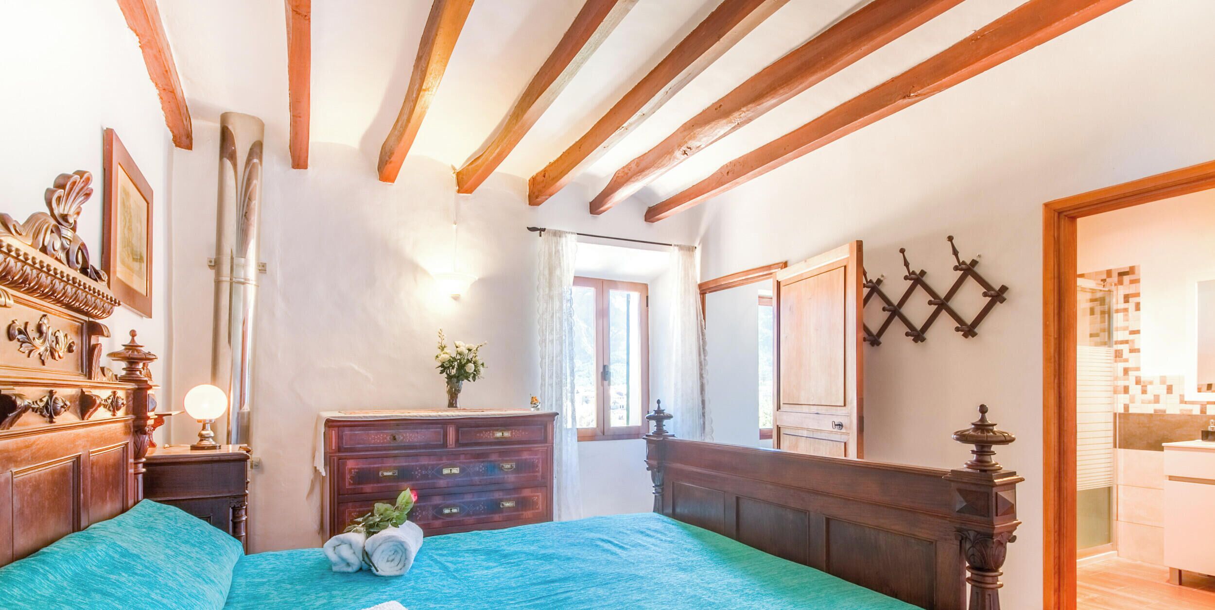 A bedroom with a large bed, wooden headboard, a dresser, a mirror, and a window with curtains.