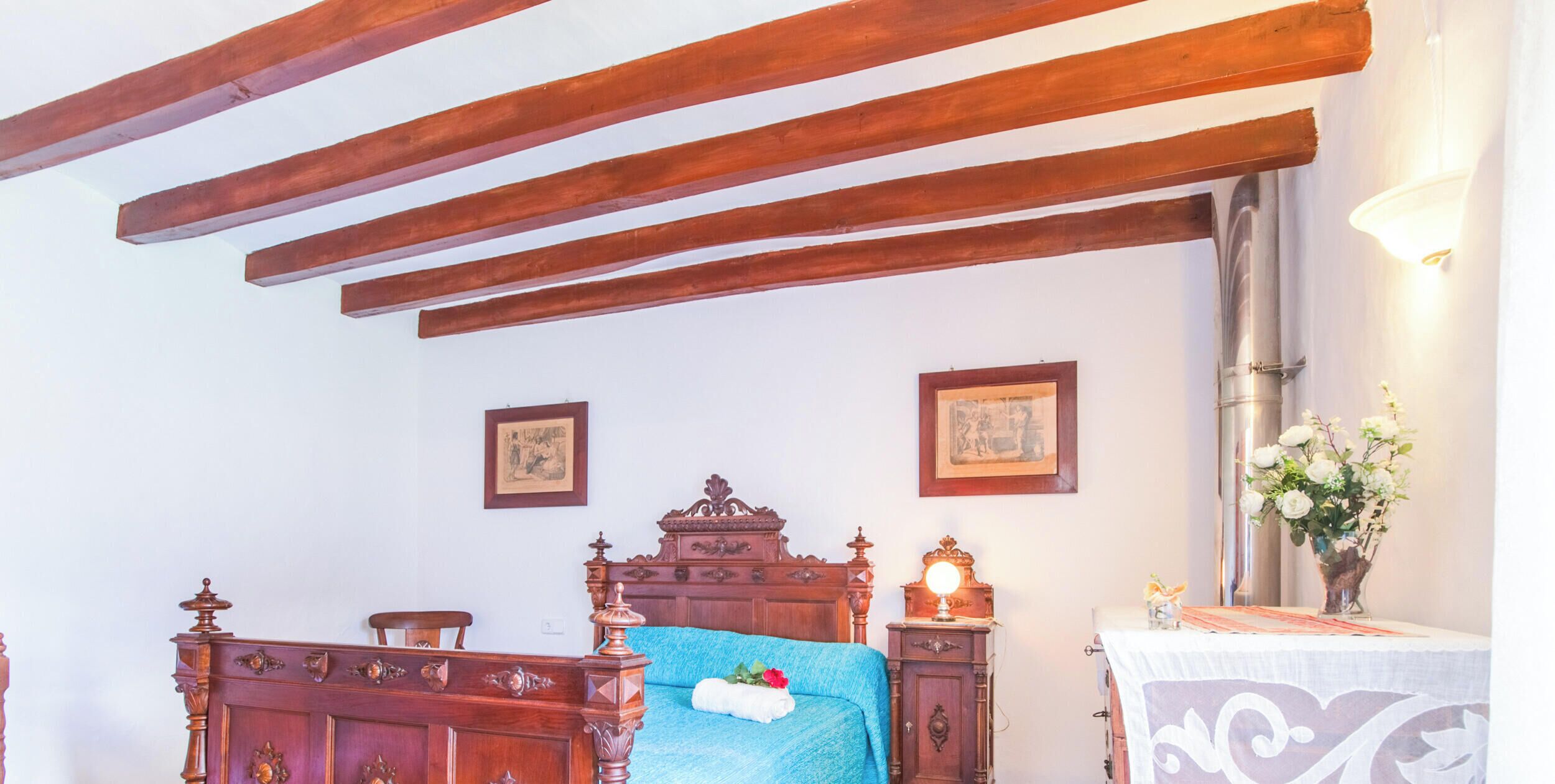 A bedroom with a wooden bed, a bedside table with a lamp, and a small cabinet.