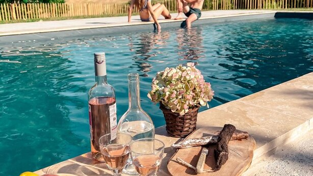 A poolside setting with a bottle of wine, glasses, and a basket of flowers on a table.