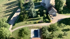 An aerial view of a castle with surrounding buildings, a swimming pool, and well-maintained lawns.