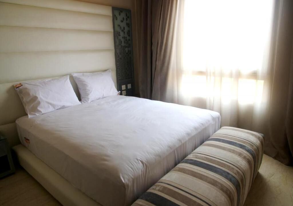 Un lit bien fait, avec du linge de lit blanc, une table de chevet et un coussin à rayures.
