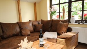 Un sofá de cuero marrón con una mesa de centro de madera, una silla de mimbre y una ventana con flores y un jarrón.