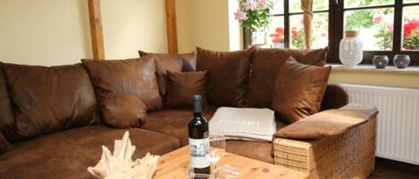 A brown leather sofa with a wooden coffee table in front, a wicker chair, and a window with flowers and a vase.