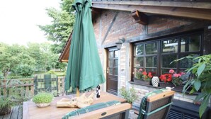Un patio al aire libre con una mesa y sillas de madera, un paraguas verde y plantas en macetas.