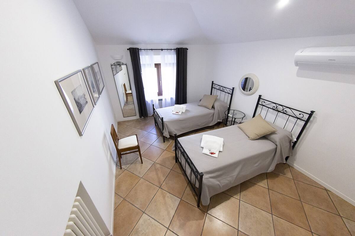 Une chambre avec deux lits, une chaise, un miroir et un climatiseur.