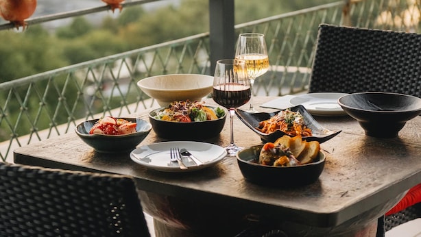 Une table à manger dressée avec différents plats et des verres de vin, le tout mis en valeur par un décor urbain en arrière-plan et des décorations à base de grenades.