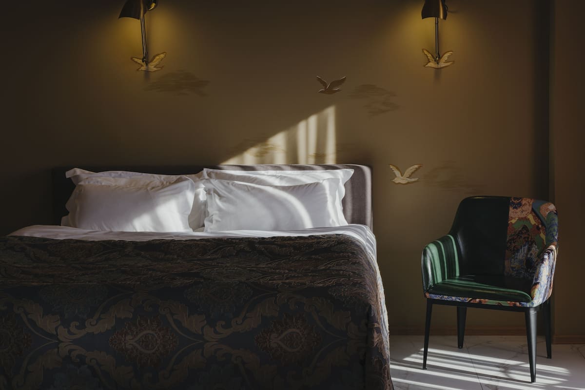 A bedroom with a bed, two wall-mounted lamps, a chair, and wall decals.