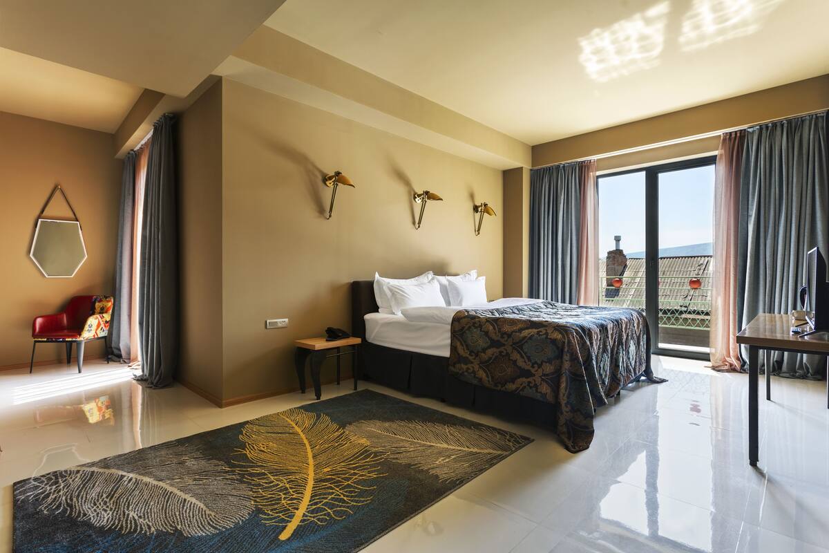 A hotel room with a bed, a desk, a chair, a large window, and a view of the outdoors.