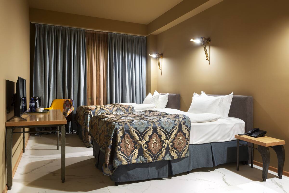 A hotel room with a bed, bedside table, lamp, and a desk with a chair.