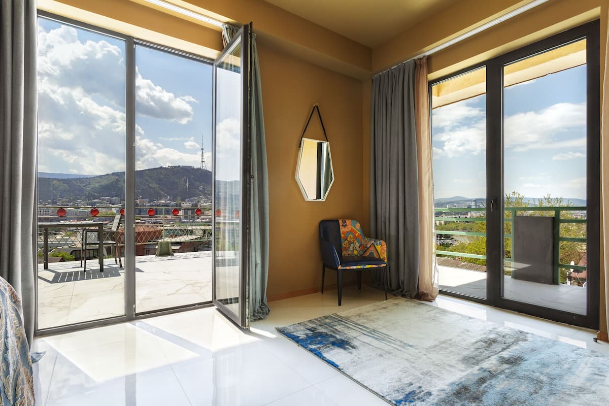 A spacious room with large sliding glass doors leading to an outdoor terrace, a comfortable chair, and a large mirror on the wall.