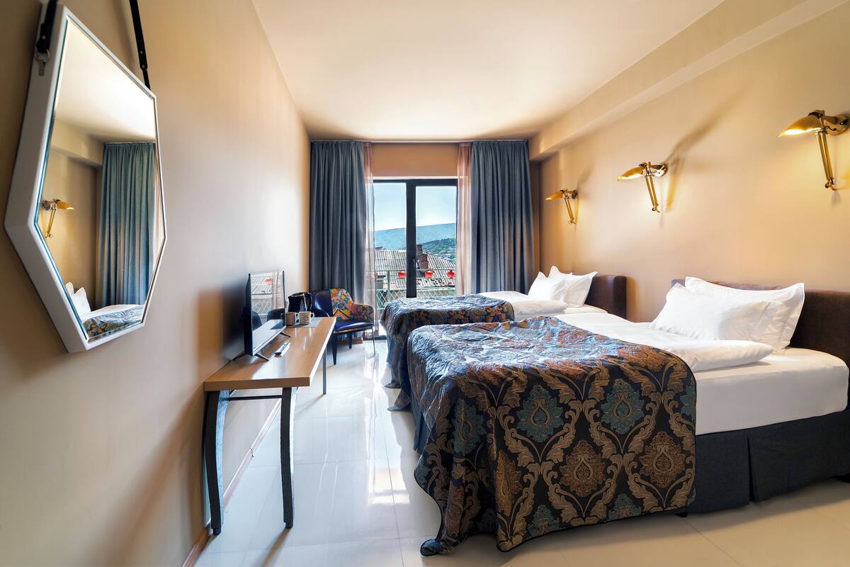 A hotel room with two beds, a desk, a mirror, and a view of the mountains.