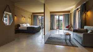 Une chambre d’hôtel spacieuse, dotée d’un grand lit, d’un canapé, d’une petite table et offrant une vue sur l’extérieur grâce à de grandes fenêtres.