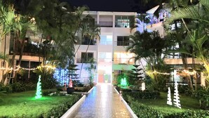 Entrada de hotel con un sendero empedrado que lleva a un edificio, rodeado de follaje y luces decorativas.