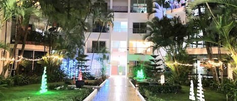 A hotel entrance with a paved pathway leading to a building, surrounded by greenery and decorative lights.