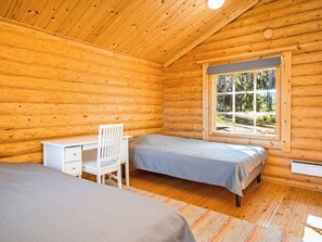 Une chambre de style rustique avec deux lits, un bureau et une fenêtre donnant sur la forêt.