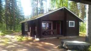 A rustic cabin with a porch, surrounded by tall trees.
