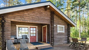 Eine Blockhütte mit Veranda, zwei Türen, einem Fenster und Gartenmöbeln.