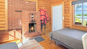 Ein gemütliches Blockhauszimmer mit Kamin aus Backstein, einem Bett, einem Fenster mit Aussicht und einem an der Wand befestigten Kleiderhaken.