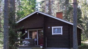 A small, single-story cabin with a porch, surrounded by trees.