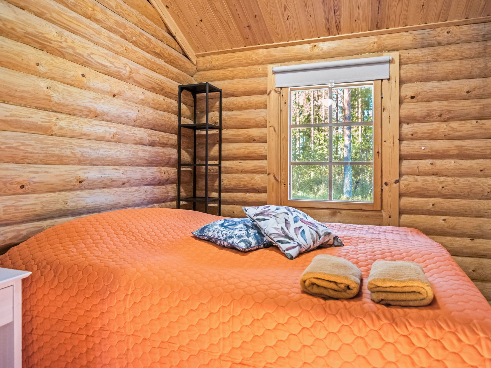 Quarto de cabana de tronco com cama, almofadas, escada e janela.