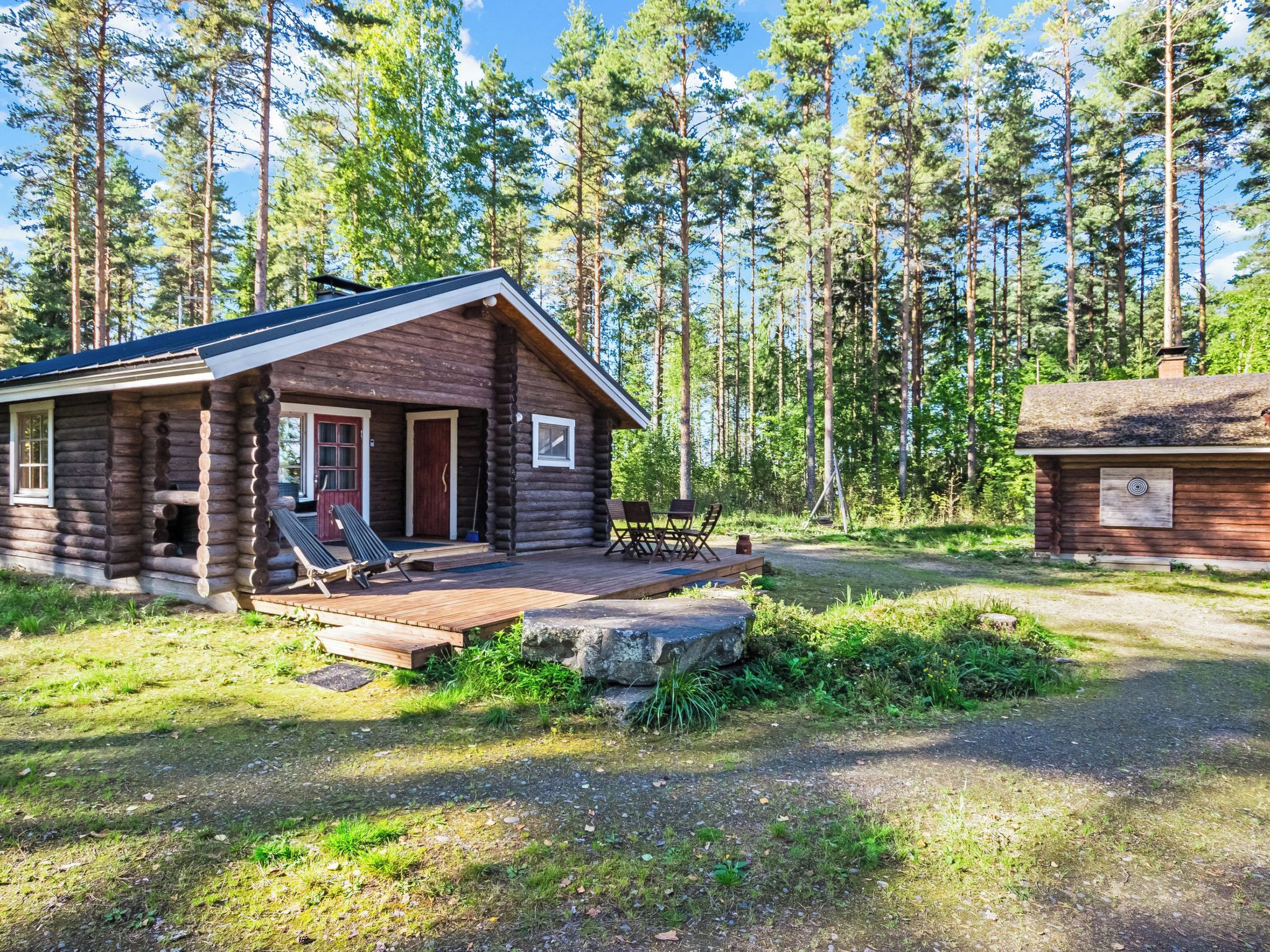A log cabin with a deck and outdoor seating, surrounded by a forest.