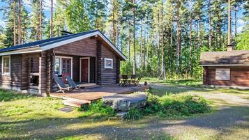 A log cabin with a deck and outdoor seating, surrounded by a forest.