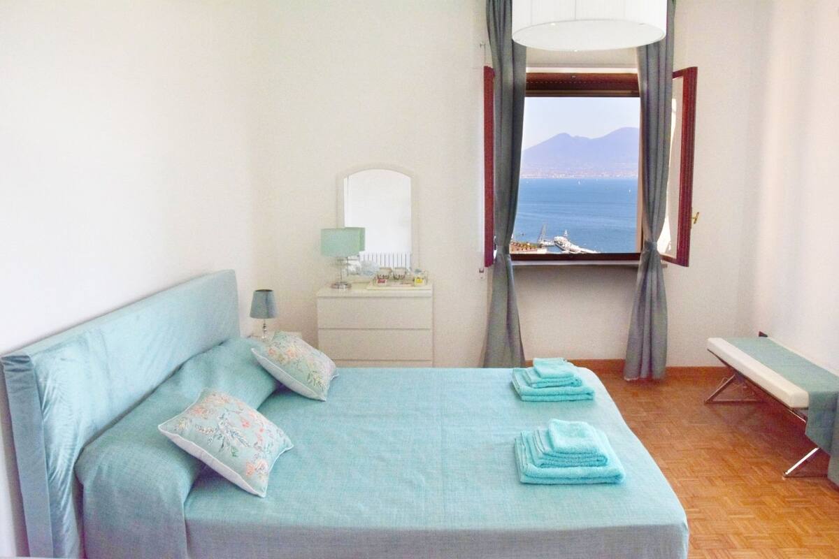 Une chambre à coucher avec un lit, une table de chevet, un miroir et une vue sur la mer.