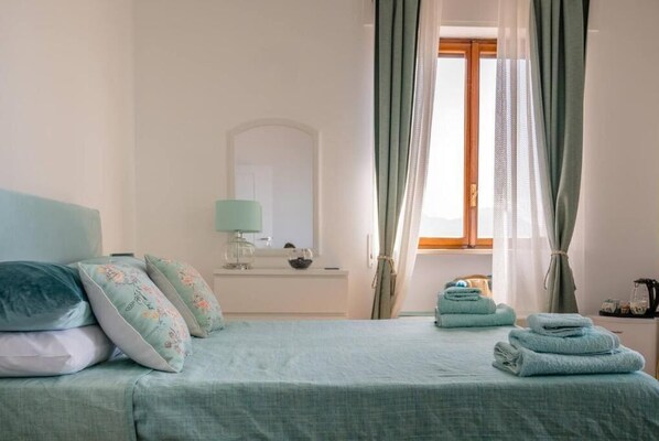 A bedroom with a bed, pillows, a bedside table, a lamp, and a window with curtains. - La Stella dei venti (Naples)