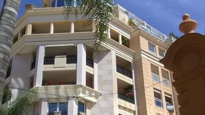 A multi-story building with balconies, a palm tree, and clear skies.