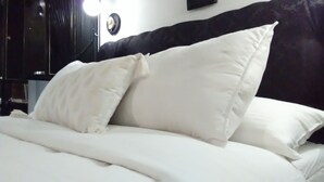 A neatly made bed with white bedding and pillows, a dark headboard, and a wall-mounted clock.