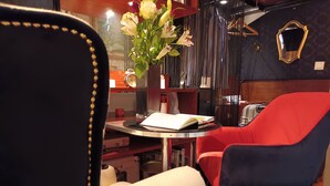 A room with a red and blue chair, a small round table with a book, and a vase with flowers.