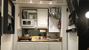 A compact kitchen with white cabinets, a microwave, and a kettle.