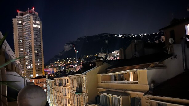 A nighttime view of a cityscape with a prominent high-rise building and a series of traditional buildings with balconies.