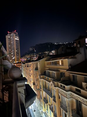 Une vue nocturne d’une ville, avec un gratte-ciel imposant et une série de bâtiments traditionnels dotés de balcons.