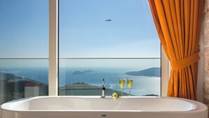 Een badkamer met een groot bad, een raam met uitzicht op zee en een fles champagne.