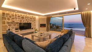 Een moderne woonkamer met een stenen muur, een flatscreen televisie, een bank, een salontafel en uitzicht op de oceaan.