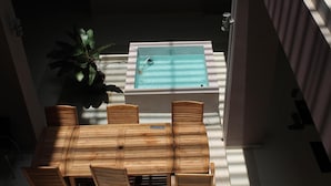 A wooden table and chairs in a sunlit outdoor area with a pool. - Hotel Amalia Malioboro (Yogyakarta)