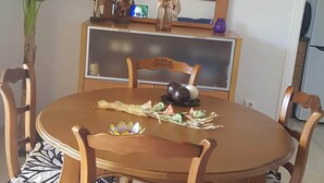 Un coin repas avec une table ronde en bois, six chaises en bois dotées de coussins à motifs zébrés, un grand miroir au-dessus de la table et une plante en pot placée à gauche.