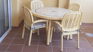 Une petite terrasse extérieure avec une table ronde et quatre chaises, entourée d’un sol carrelé.