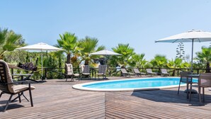 Una terraza de madera con piscina, sillones de descanso y sombrillas.