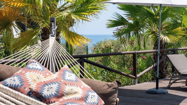 Una hamaca con almohadones estampados, una silla de descanso y una terraza de madera con barandilla con vista al océano.