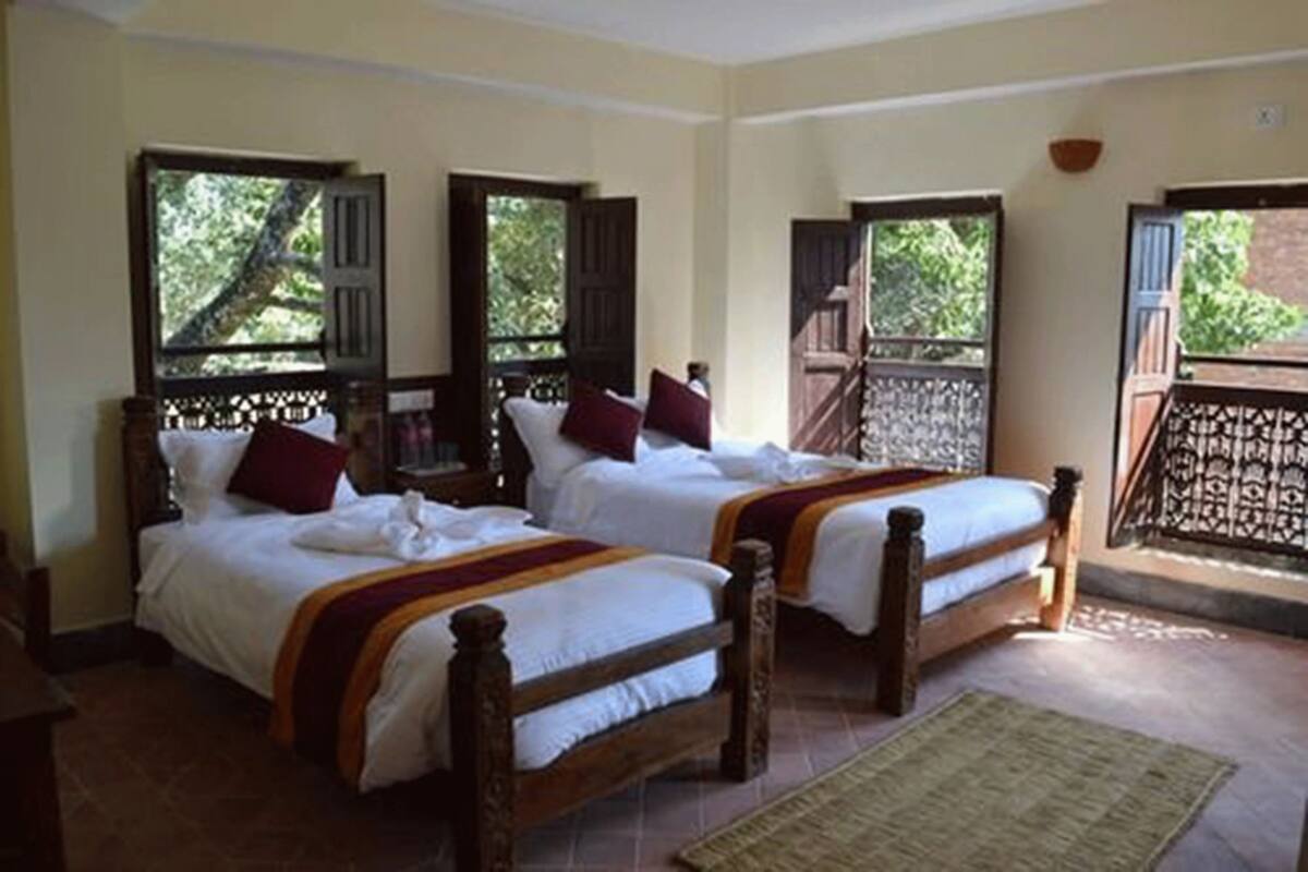 A room with two wooden beds, each with white bedding and red pillows. There are windows with wooden shutters, and a balcony with a decorative railing.