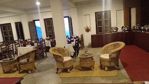 A dining area with wicker chairs, round tables, and a red carpet.