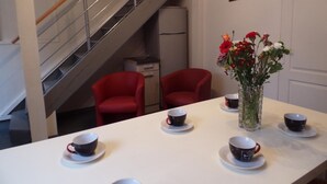 A dining area with a white table set for four, red chairs, a vase with flowers, and a staircase in the background. - Contemporary 3-level house in Vaumas, near Moulins (Vaumas)