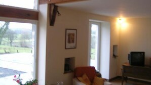A room with a large window, a wooden ceiling beam, a framed picture on the wall, and a television on a wooden stand. - Modern Rustic Cottage with Pool and Pets Allowed (Chirat-l'Église)